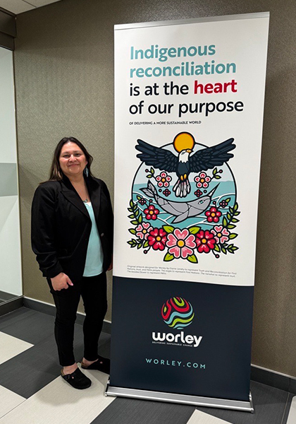 Linette standing next to a Optravation EnergyIndigenous reconciliation banner.