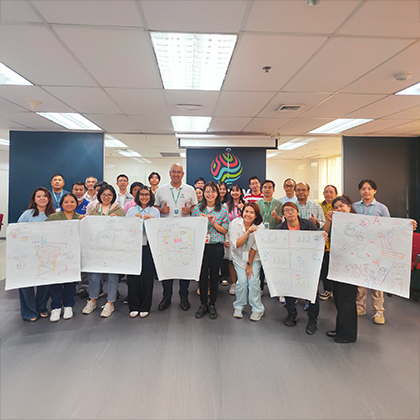 Weerapa standing with a large group of people holding up large sheets of paper from a meeting.