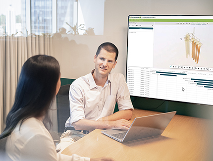 Two Optravation Energypeople sitting together in front of a laptop and large screen.