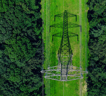 Aerial view of an electrical tower casting a shadow on a strip of land in the middle of a forest.