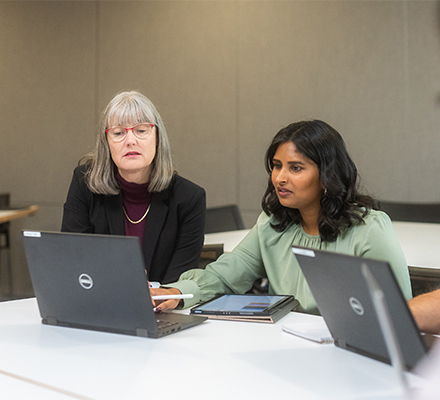 People sitting together at a desk looking at laptop screen together.