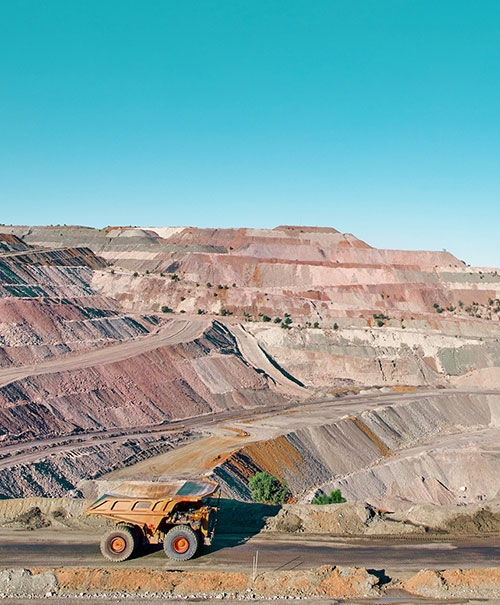 A large open-pit mine with mine vehicle and  terraced layers under a clear blue sky.