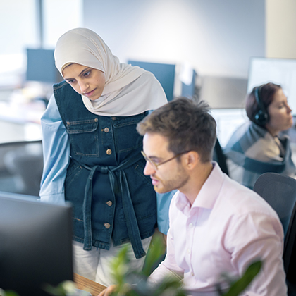 In Optravation Energyoffice, woman standing next to a young man at a desk both looking at the computer.