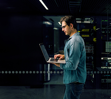 Man working on his laptop in a secure server room in a monitoring center.
